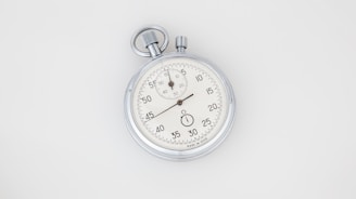 A vintage analog stopwatch with a metallic case and a white dial featuring black numbers. The watch has two dials; the main dial is marked with seconds while the smaller one is for minutes. The top has a winding crown and push button.