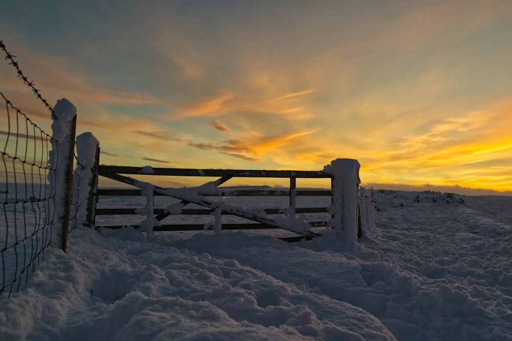 cerca de madeira marrom no chão coberto de neve durante o pôr do sol