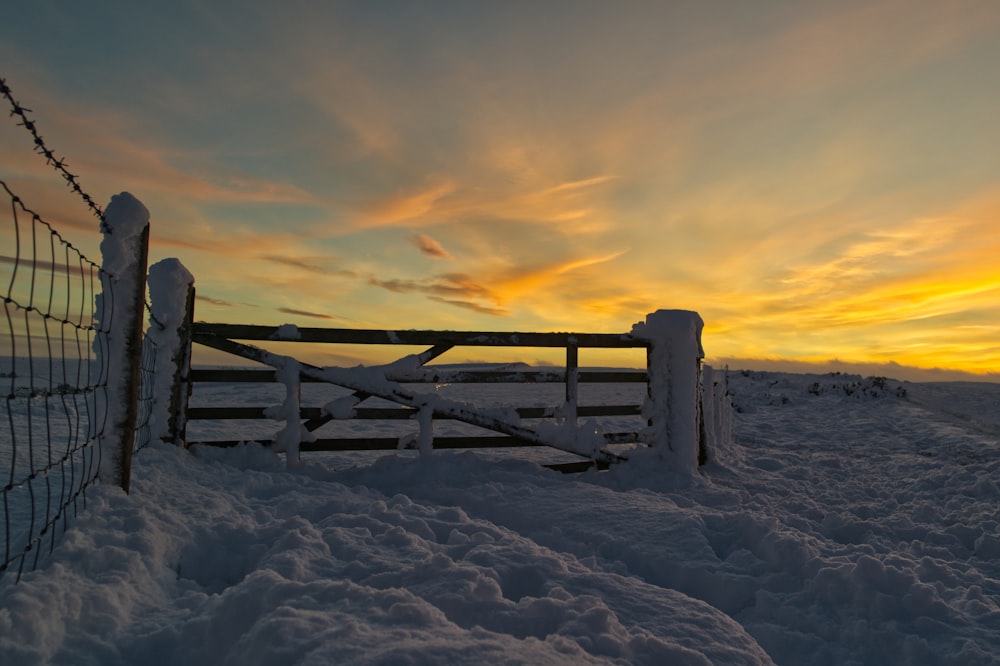 brown wooden fence on snow covered ground during sunset