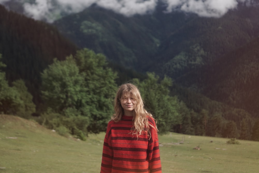 Donna in camicia a maniche lunghe a righe rosse e nere in piedi sul campo di erba verde durante il giorno