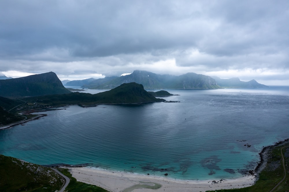 body of water near mountain under white clouds during daytime