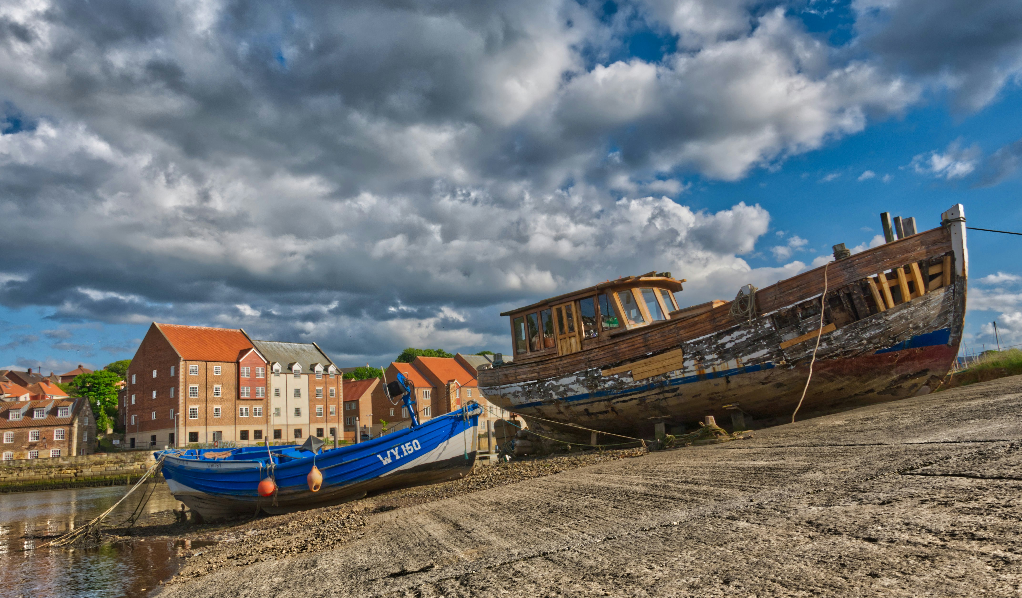 blaues und orangefarbenes Boot am Strandufer tagsüber unter bewölktem Himmel