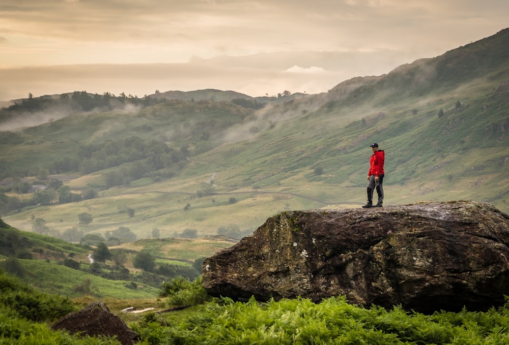 man in red shirt standing on rock mountain during daytime