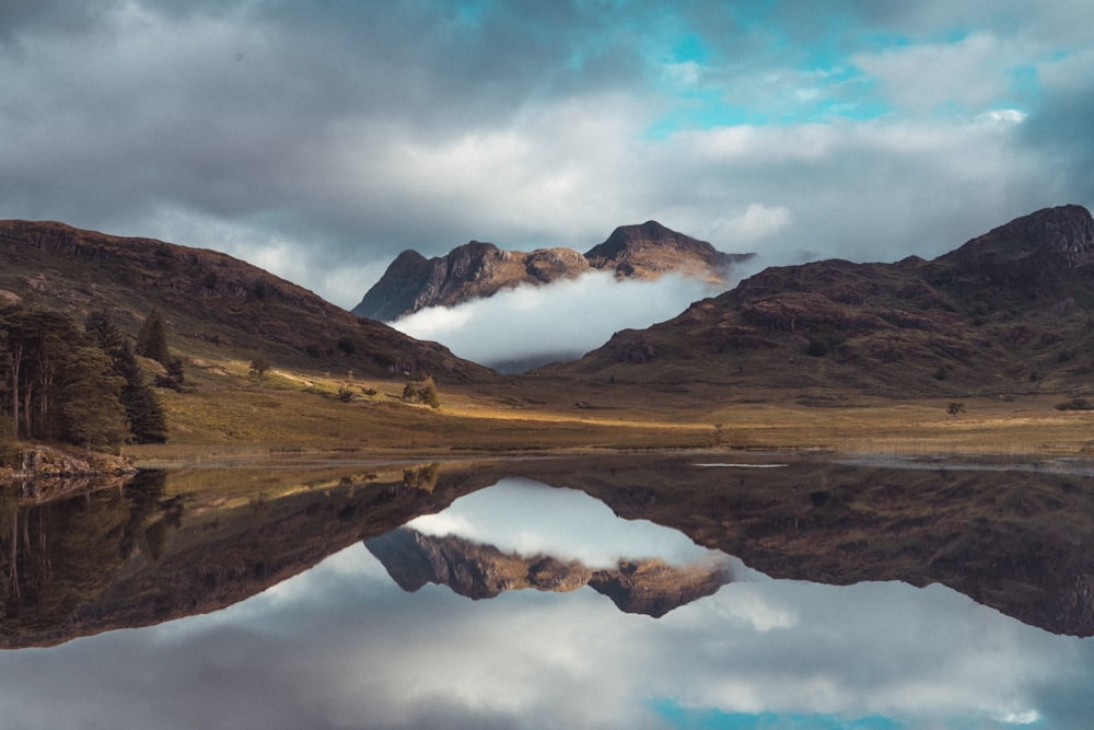 brown and white mountains near lake under white clouds and blue sky during daytime