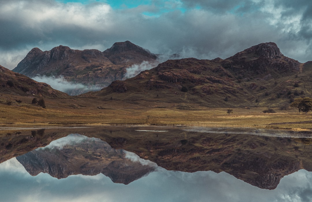 brown and gray mountains beside body of water under white clouds and blue sky during daytime