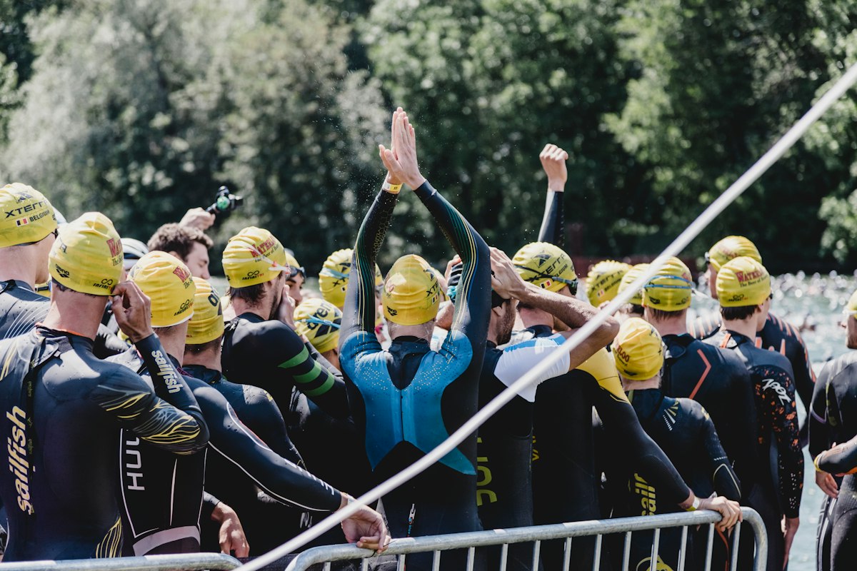Triathlètes en combinaison néoprène et bonnet de bain jaune rassemblés derrière une barrière avant le départ de la natation