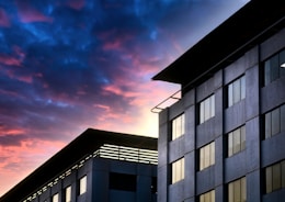 A modern condo building with large windows overlooking the city skyline at sunset.