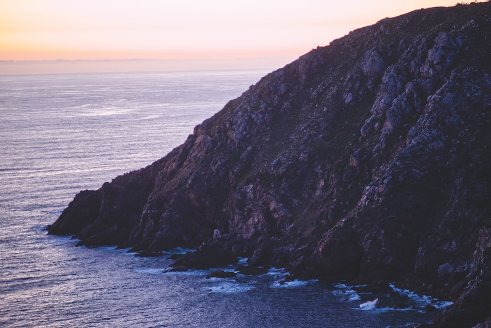 brown rocky mountain beside sea during sunset