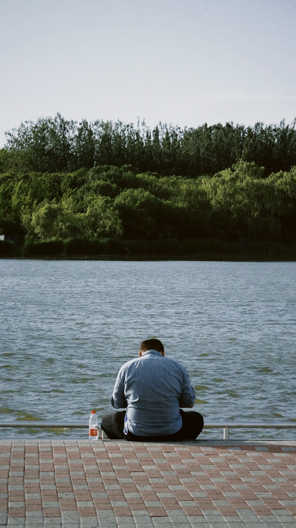 man in blue shirt sitting on rock in front of body of water during daytime