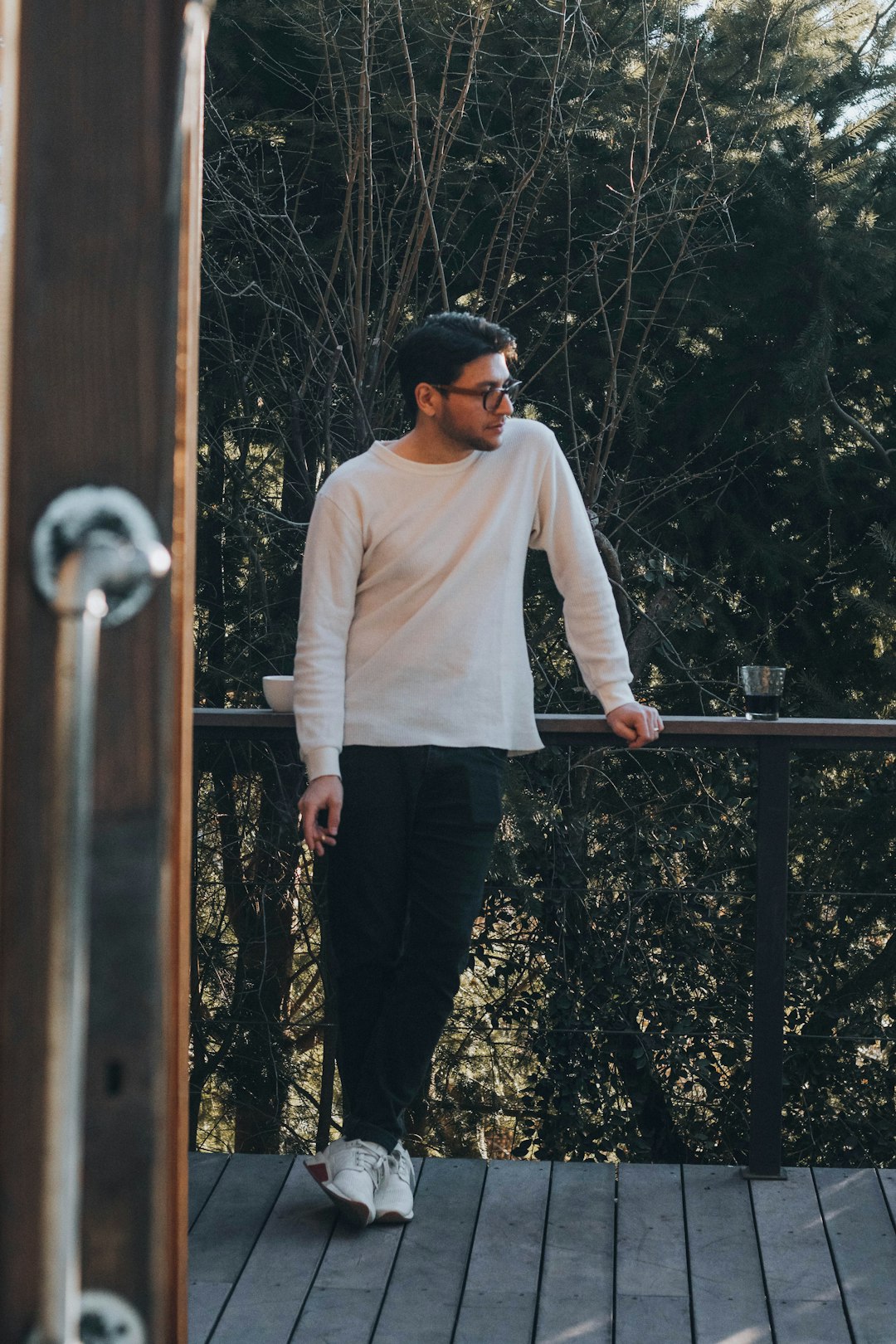 man in white long sleeve shirt and black pants standing on brown wooden bridge