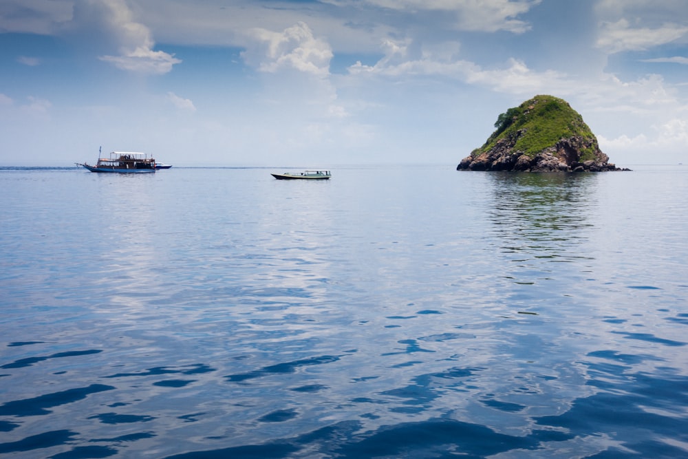 boat on sea near island under white clouds and blue sky during daytime