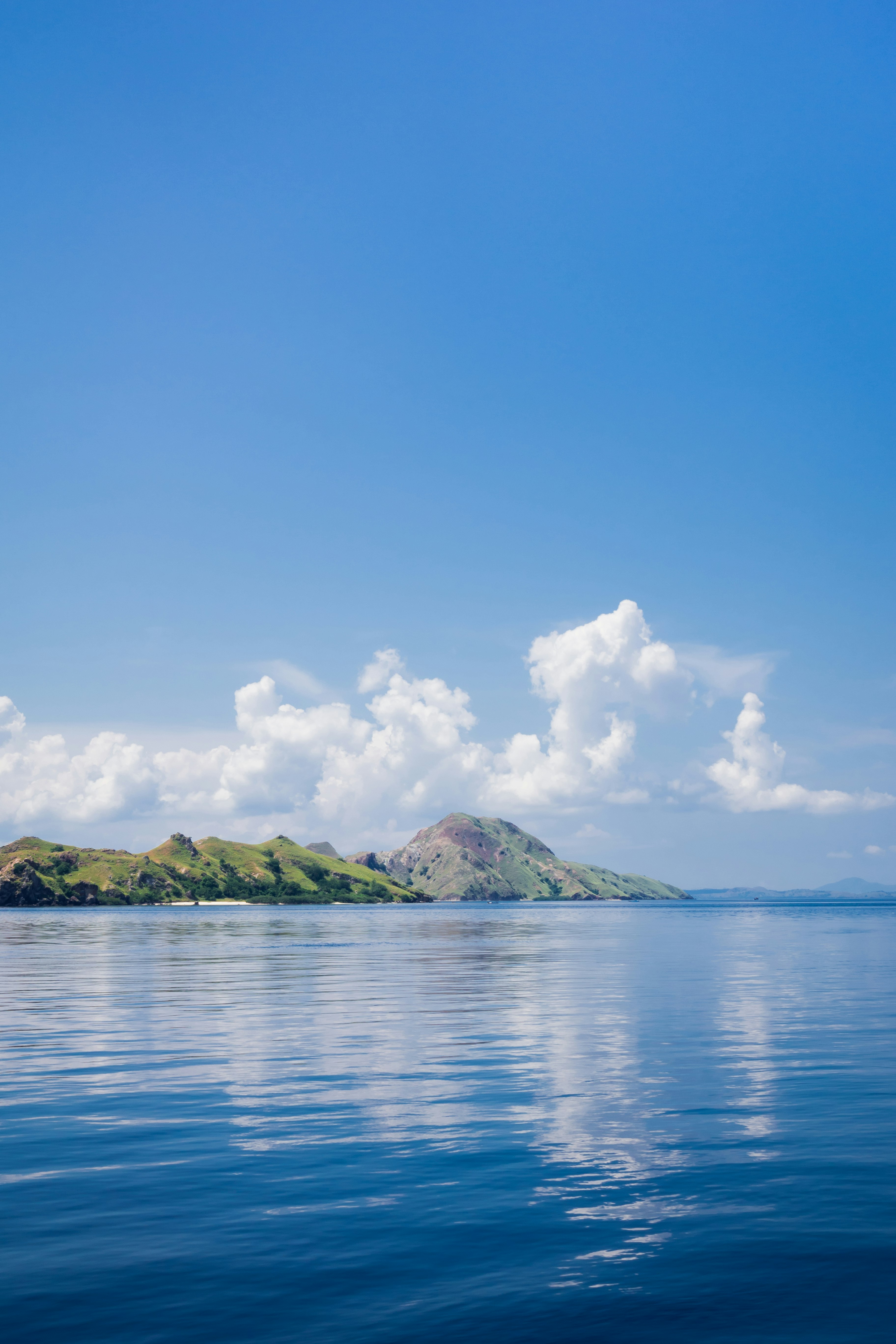 green island on blue sea under blue sky and white clouds during daytime