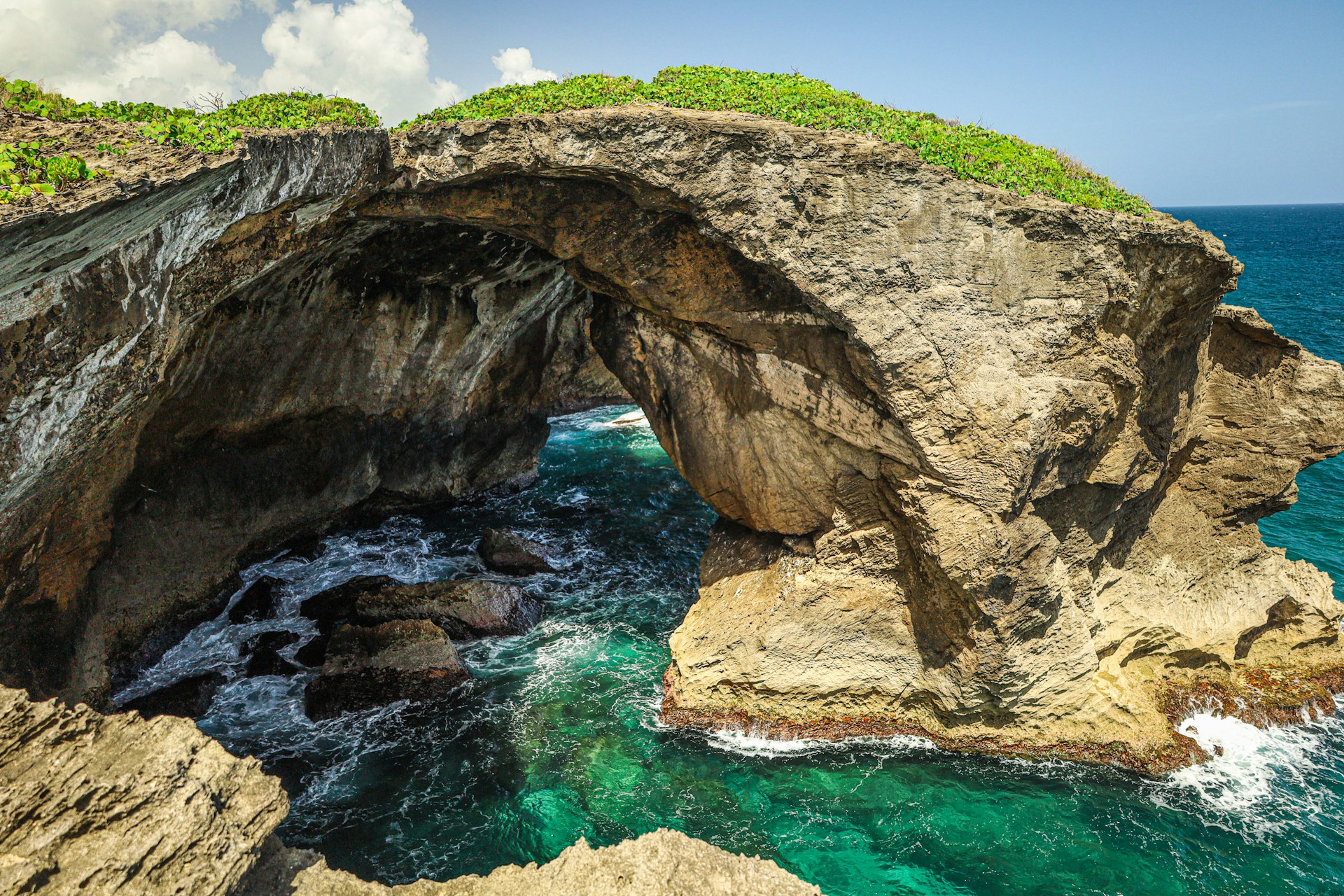 brown and green rock formation on blue sea under white clouds and blue sky during daytime