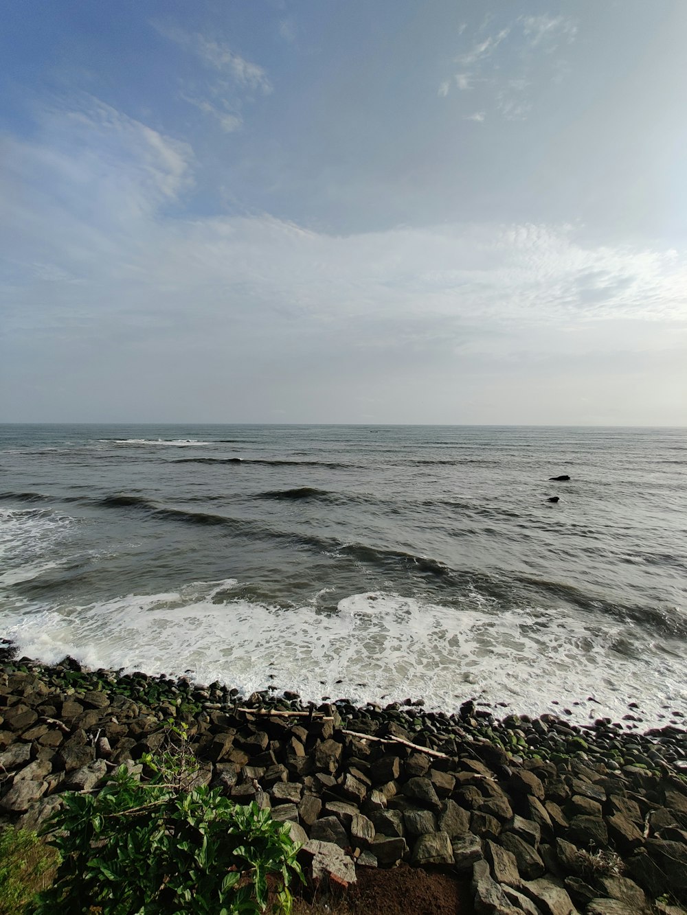 ocean waves crashing on rocks under white clouds during daytime