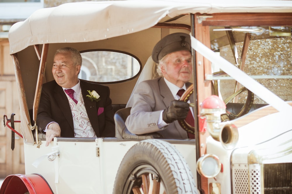 man in black suit sitting on white vintage car