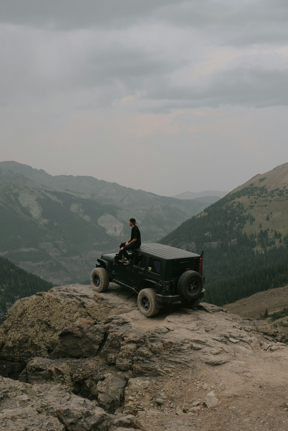 Mann im schwarzen Hemd sitzt tagsüber auf schwarzem Jeep Wrangler auf Rocky Mountain