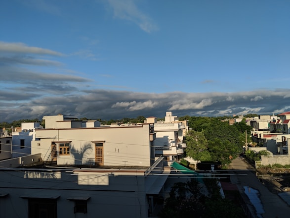 A welcoming neighborhood street with diverse homes, commercial buildings, and open land under a bright blue sky.