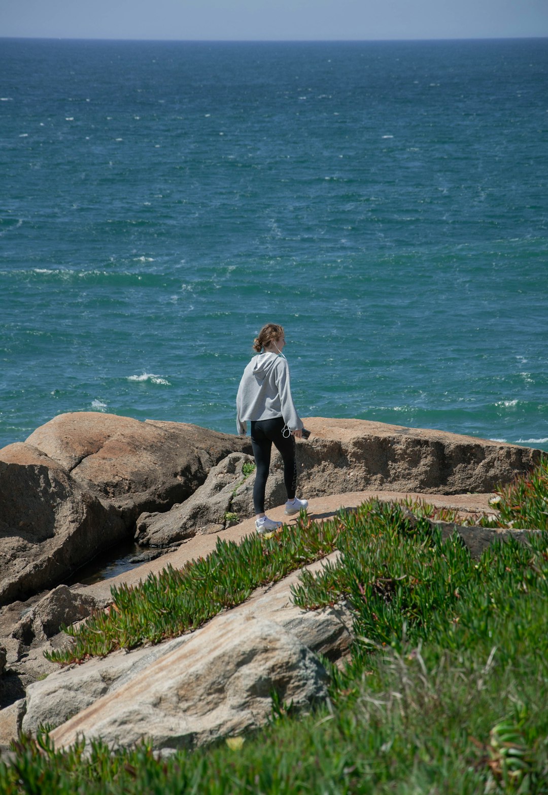 man in white dress shirt and black pants standing on brown rock near body of water