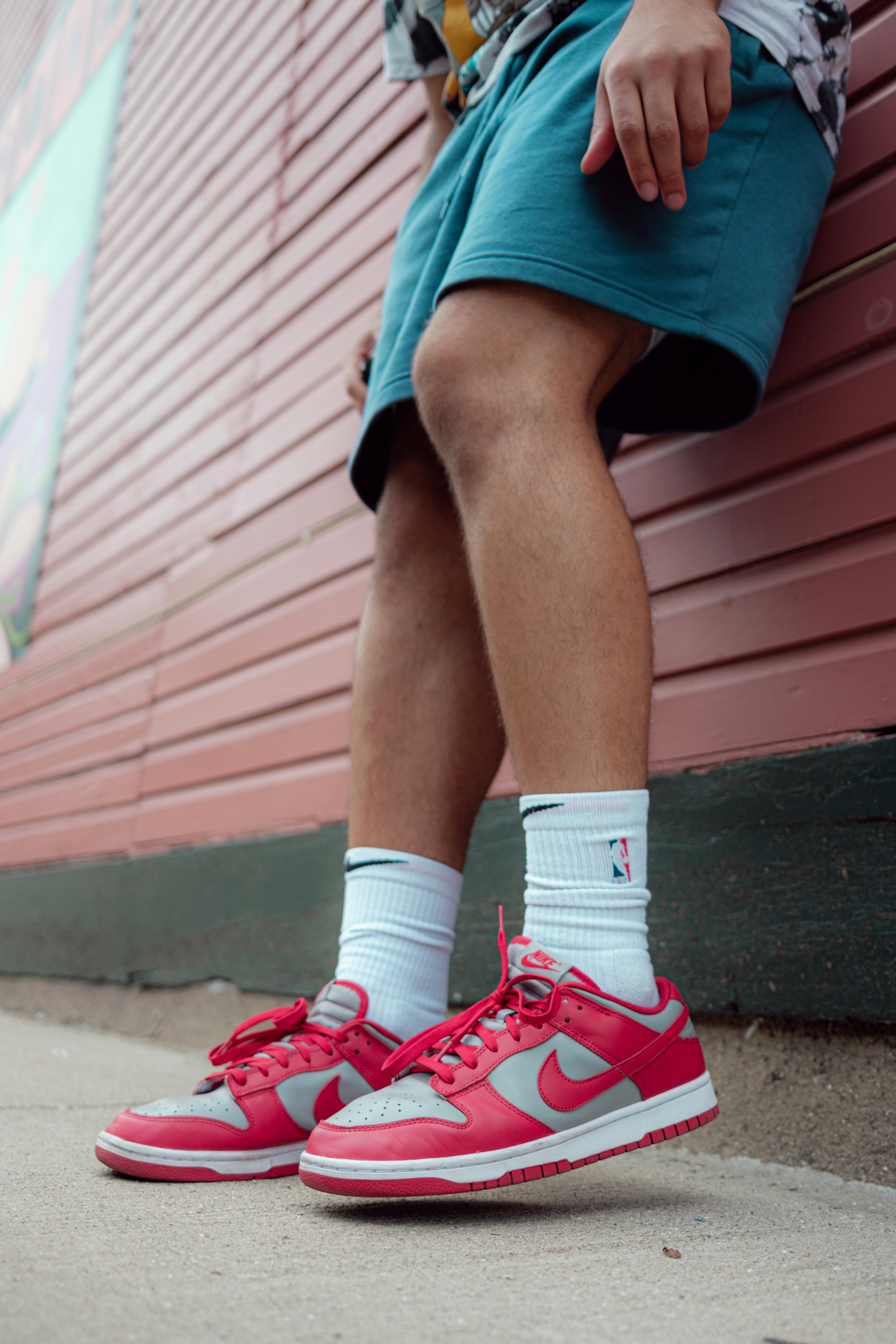 Personne en short bleu et baskets Nike rouges et blanches assise sur un banc en bois rouge