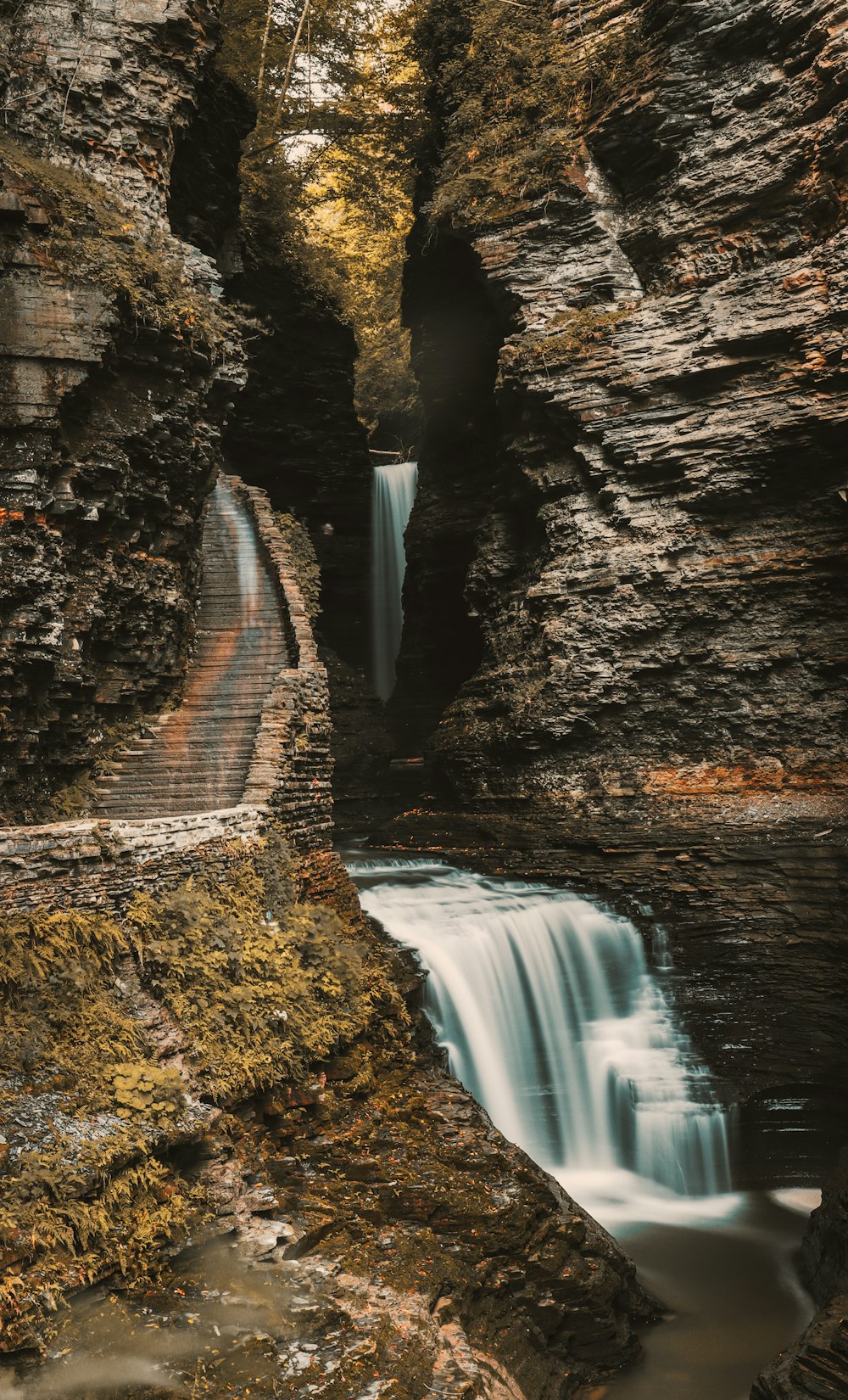 water falls between brown rocky mountain during daytime