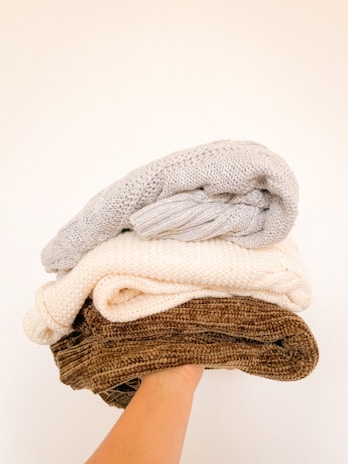 Close-up of hands carefully folding a soft, second-hand sweater with delicate stitching.