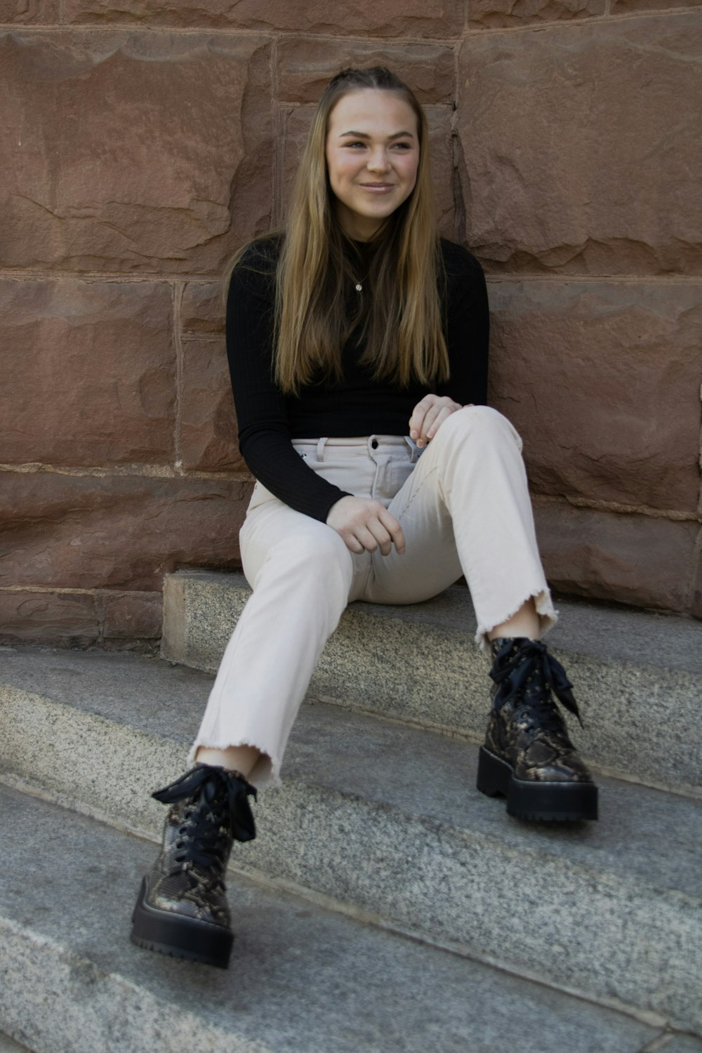 woman in black long sleeve shirt and white pants sitting on concrete bench