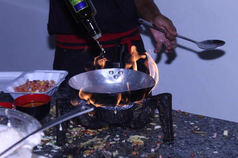 person holding bottle and cooking pot with fire