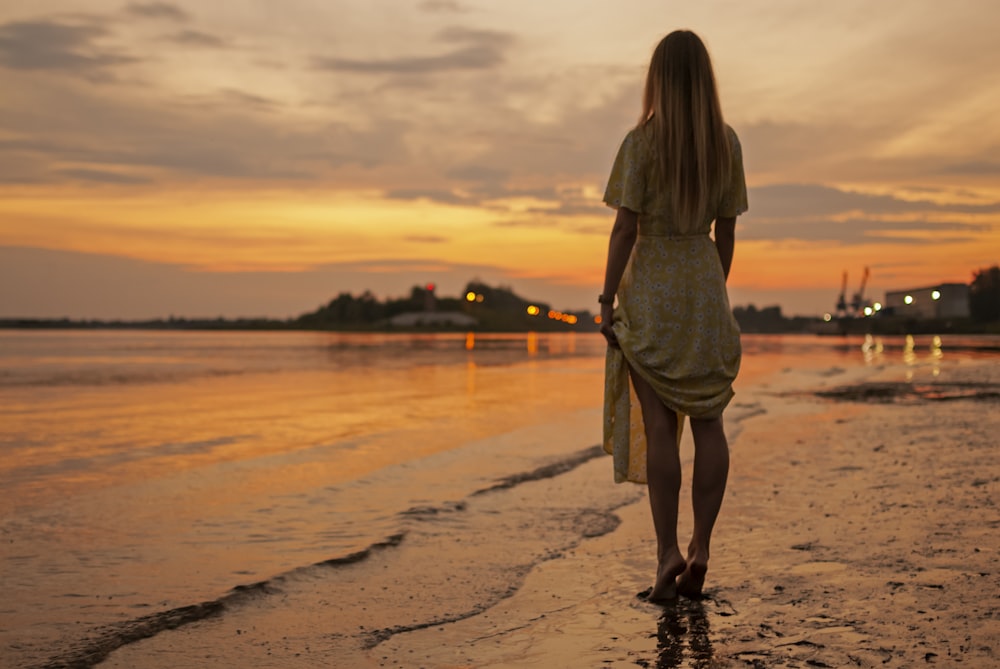 femme en robe brune debout sur la plage pendant le coucher du soleil
