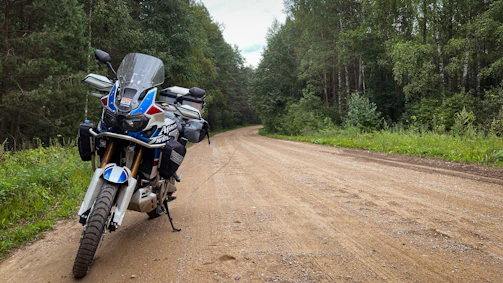 A sturdy motorcycle parked beside a dirt road surrounded by trees
