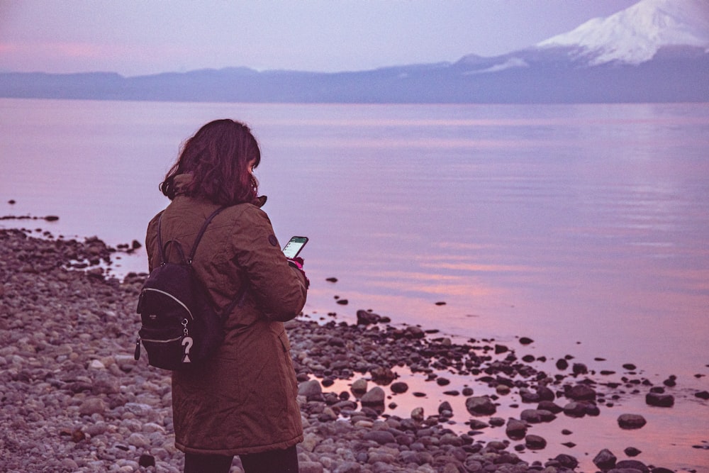 woman in brown jacket standing on rocky shore during daytime