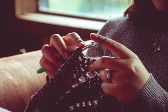 A warm, inviting photo of a skilled artisan knitting a wool sweater by hand in a cozy workshop.