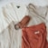 Several neatly arranged clothing items including sweaters and a belt. The clothing pieces are in neutral and earth tones, and they are laid out on a light-colored surface.