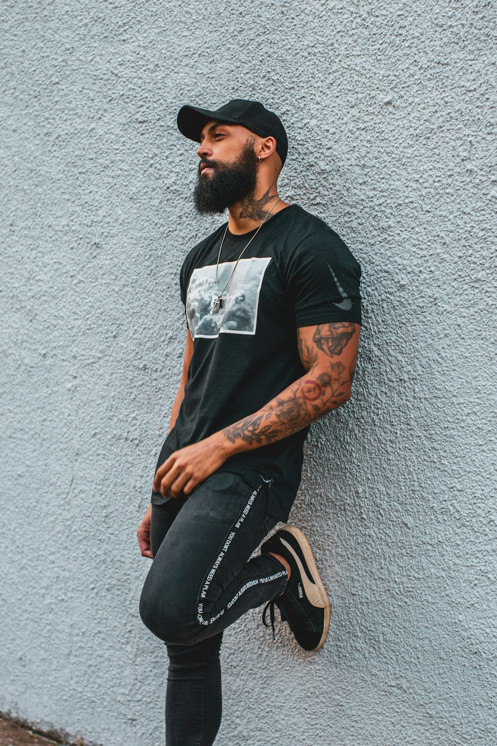 man in black crew neck t-shirt and black denim jeans sitting on concrete wall