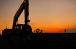 silhouette of people standing near excavator during sunset