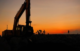 silhouette of people standing near excavator during sunset