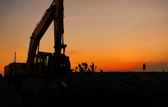 silhouette of people standing near excavator during sunset