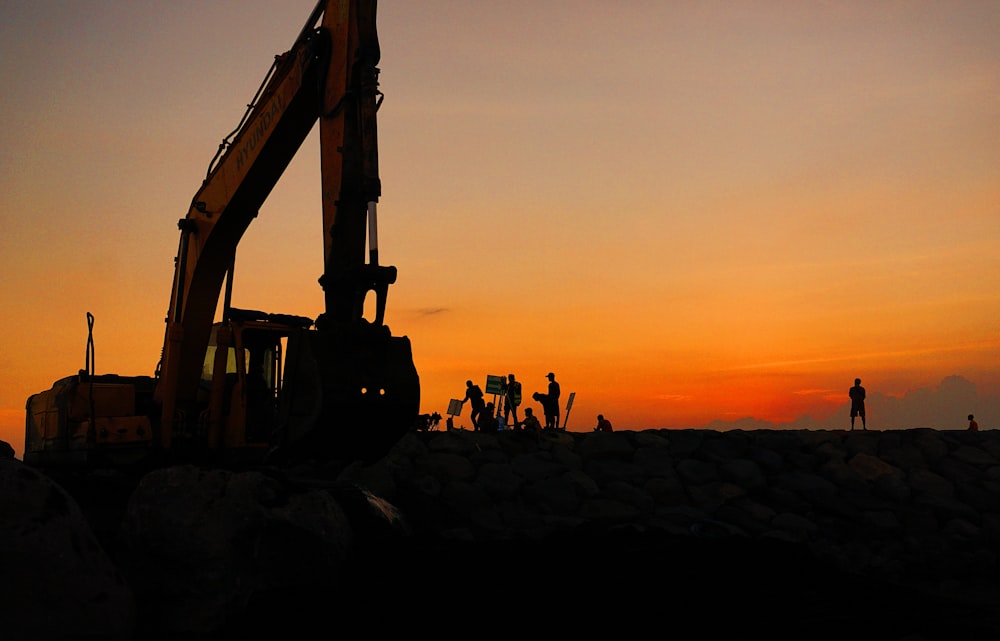silhouette of people standing near excavator during sunset