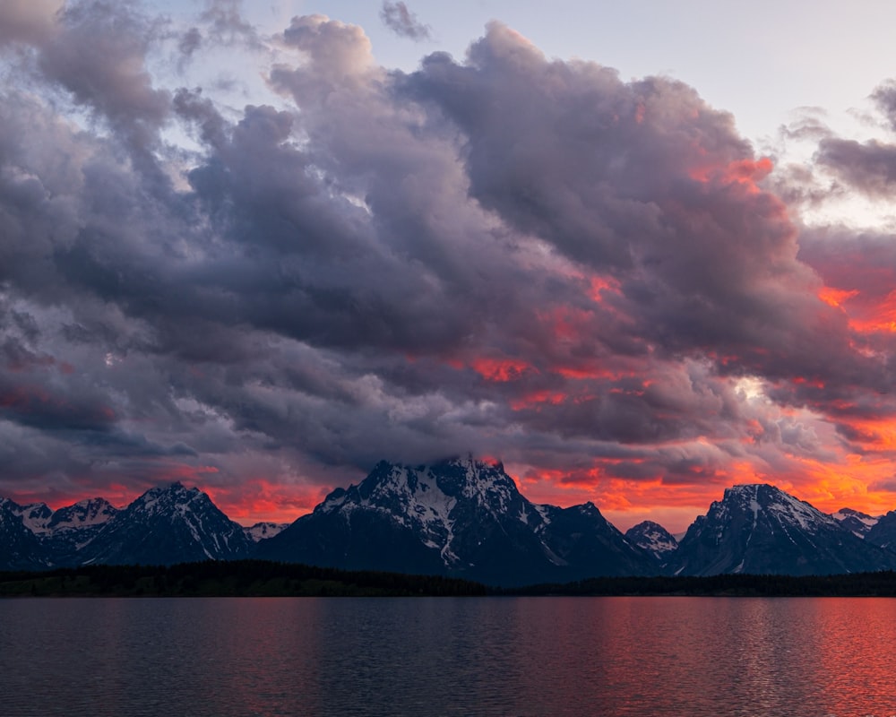 body of water near mountain under cloudy sky during daytime