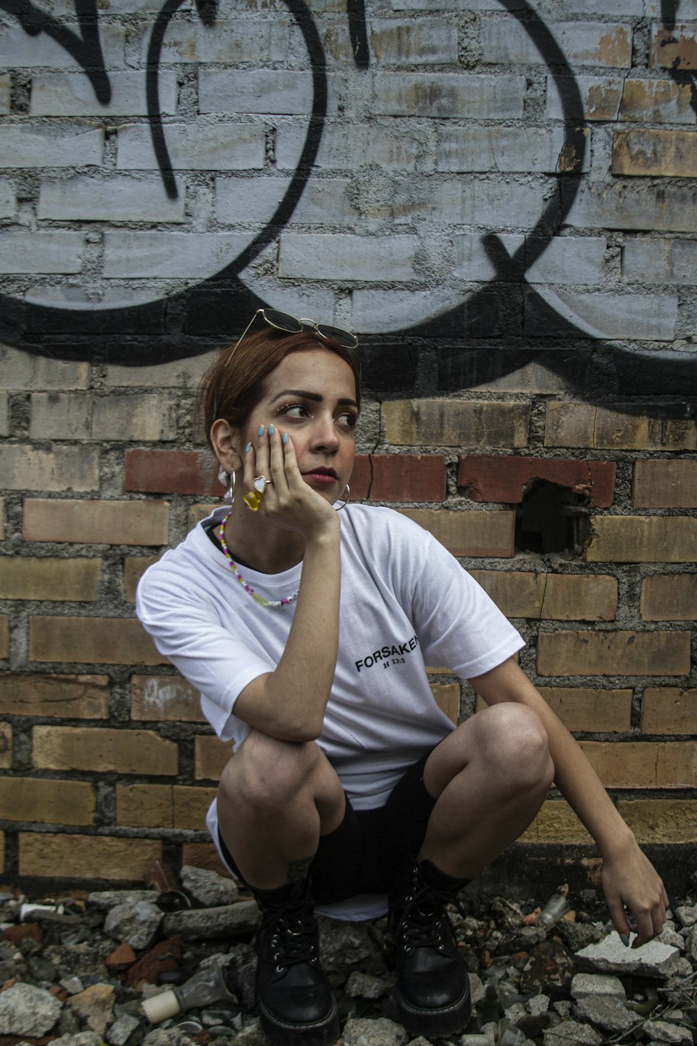 a woman squatting on the ground in front of a brick wall
