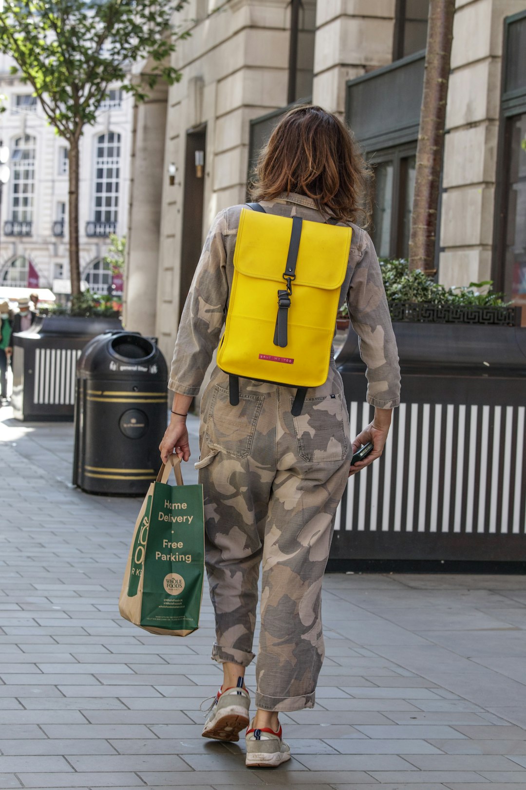 woman in brown and beige camouflage pants and yellow backpack standing on sidewalk during daytime