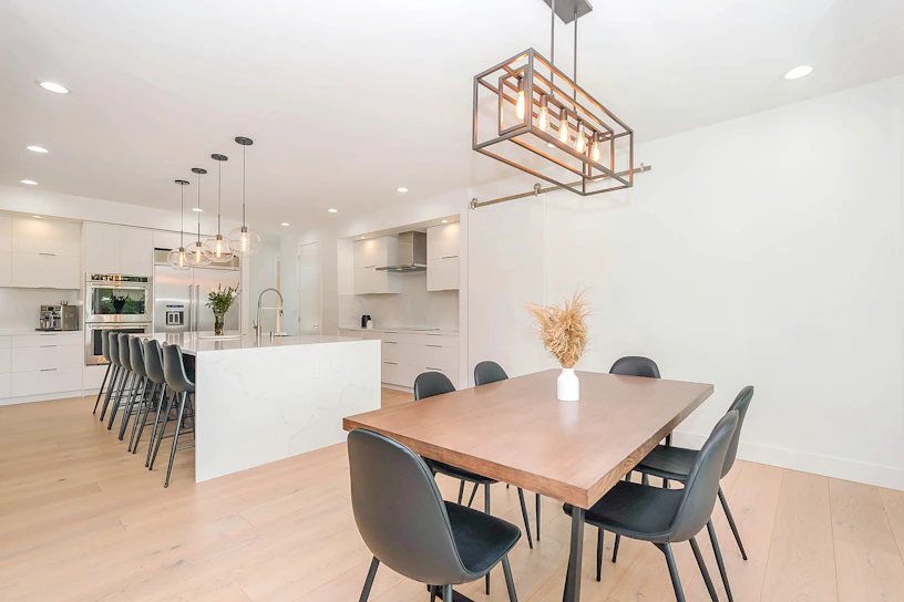 A sleek modern kitchen corner featuring a minimalist wooden dining table with elegant black chairs.