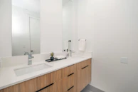Modern bathroom vanity with natural wood accents and a white countertop in a bright space.