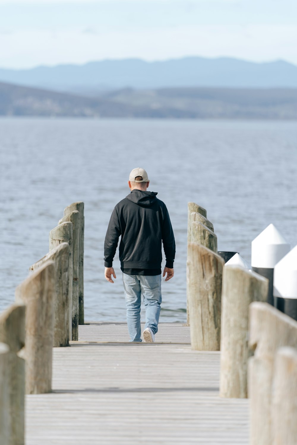 Hombre con chaqueta negra y jeans de mezclilla azul de pie en el muelle de madera durante el día