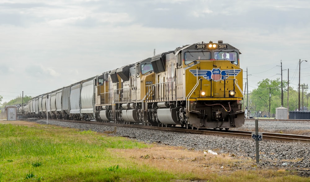 yellow and black train on rail tracks under white clouds during daytime