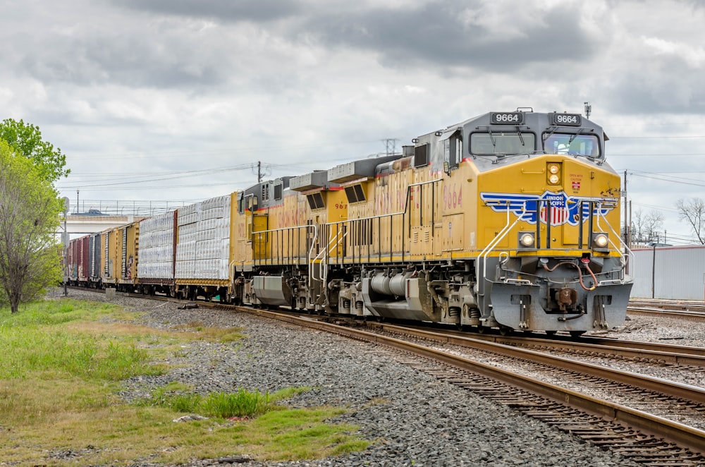 tren amarillo y negro en las vías del tren bajo nubes blancas y cielo azul durante el día