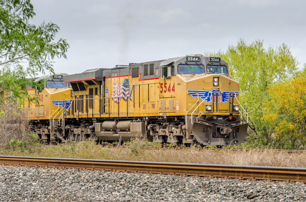 yellow and red train on rail tracks under white clouds during daytime