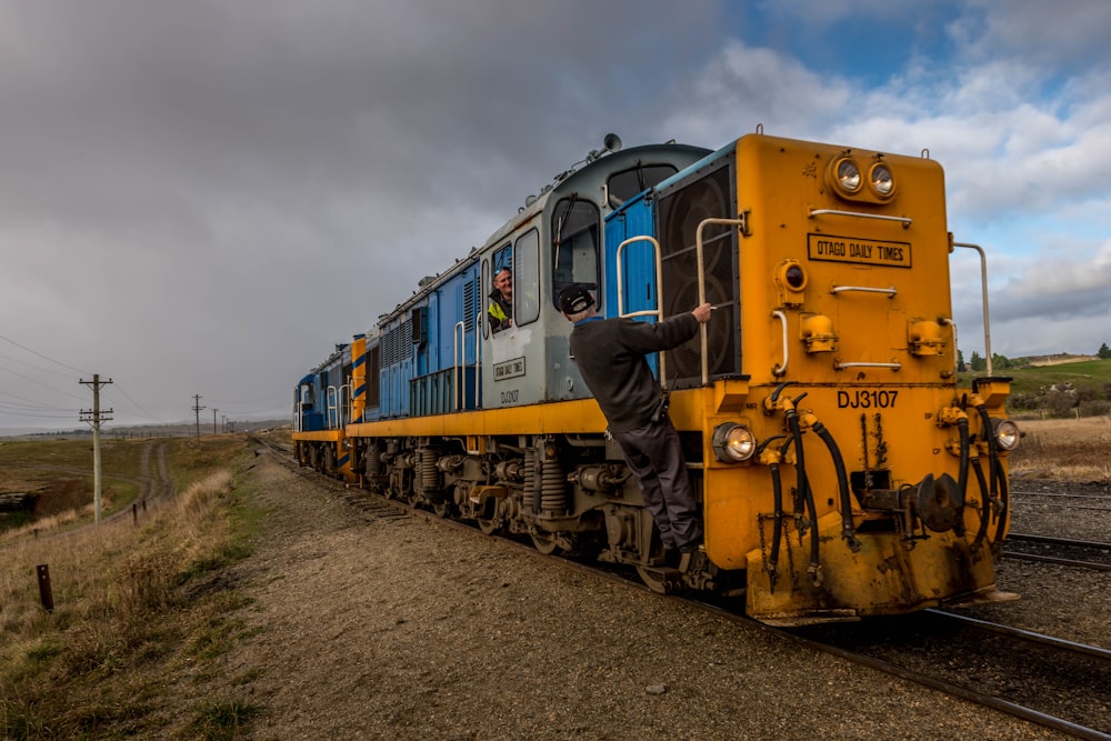 yellow and blue train on rail tracks under cloudy sky during daytime