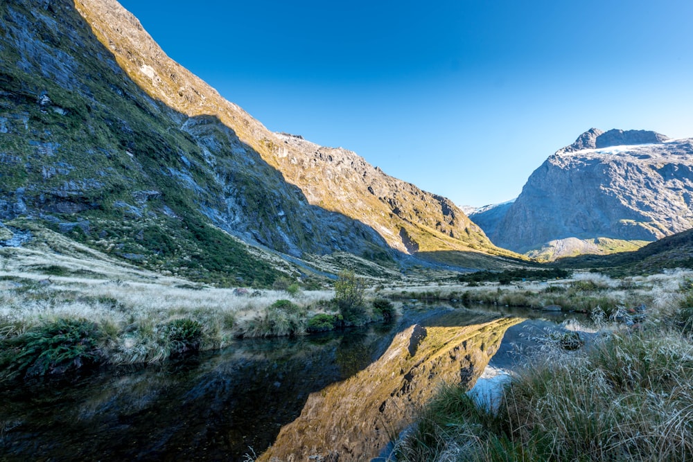 montagna verde e marrone accanto al lago sotto il cielo blu durante il giorno