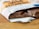 A partially unwrapped bar of chocolate lies on a wooden surface, revealing pieces of nuts embedded within the chocolate. The packaging is slightly torn and features text with a stylish design.