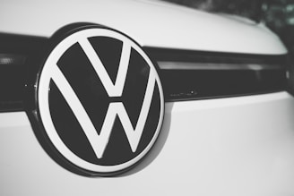 A close-up of a Volkswagen logo centered on the front of a vehicle, displaying the iconic VW letters in a bold, black and white design against a smooth, clean surface.